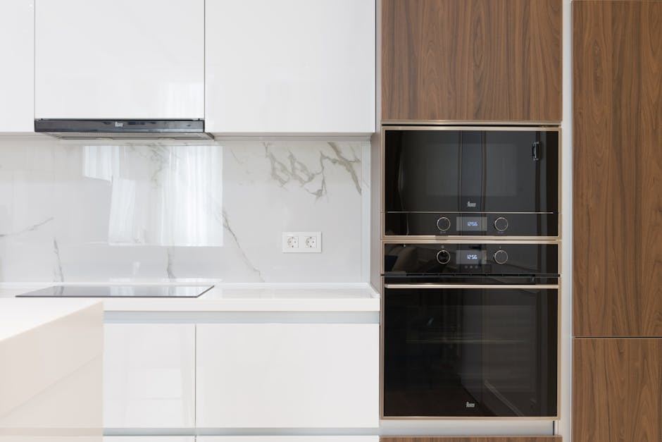 A modern kitchen surface cleaning scene featuring a white matte-finish kitchen cabinet with sleek, handleless drawers and cabinets. A stainless steel oven with a glass door and control knobs is built 